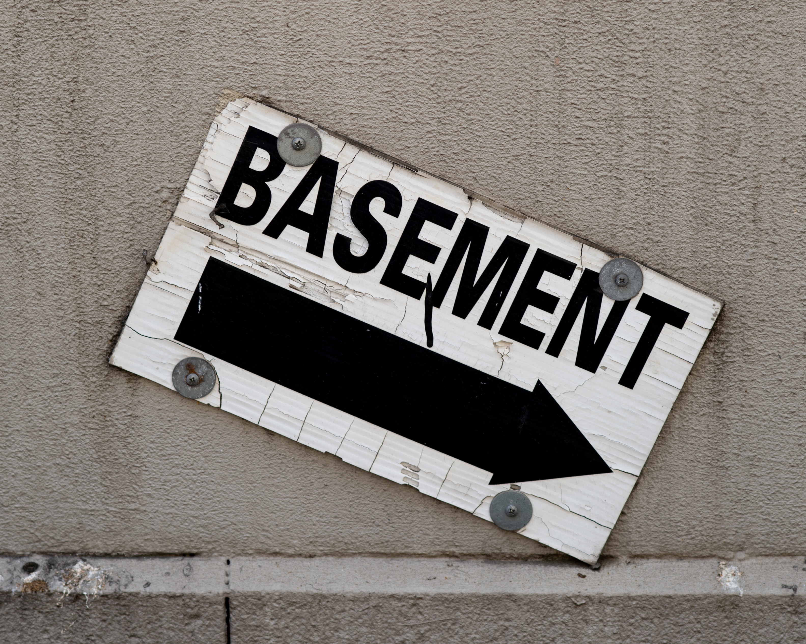 A concrete wall with a sign reads basement and an arrow that points down in black letters on white background.